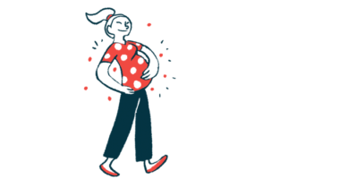 A pregnant woman is shown smiling as she walks with both hands supporting her abdomen.