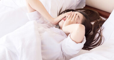 woman laying in bed with hands over her face
