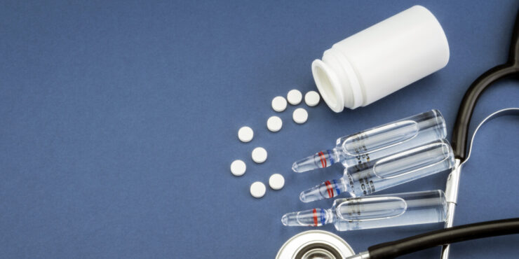 pills spilling out of a pill bottle, vials, and a stethoscope on a blue background