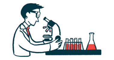 A researcher wearing safety goggles examines a sample using a microscope, alongside a rack of filled vials and a flask.