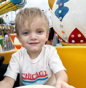 A close-up of a boy wearing a Chicago T-shirt and sitting in a large yellow teacup as part of a county fair's teacup ride. 