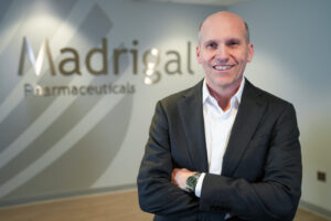 Madrigal Pharmaceuticals CEO Bill Sibold is pictured in front of a sign of the company's name.