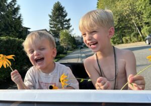 Two young boys giggle while holding yellow flowers in the summer sun. 