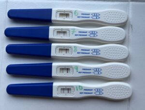 Five pregnancy test tools in blue and white, with the bottom test showing a clear two lines.