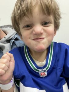 A boy with blond hair who's wearing a blue NFL shirt poses with an engaged expression.