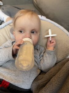 A young boy, maybe about a year old, reclines against a pillow while drinking from his bottle.