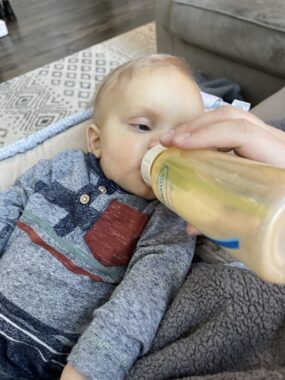 A baby boy drinks formula from a bottle that has been stained orange by a multivitamin.