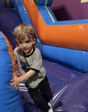 A 5-year-old boy emerges from a blue and orange bouncy castle obstacle course with a determined look on his face. 